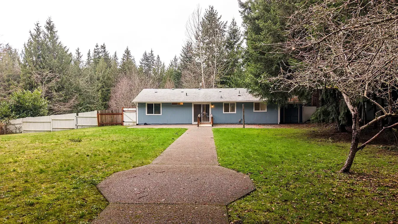 Blue house with a stone pathway leading from the yard to the front door, surrounded by trees.