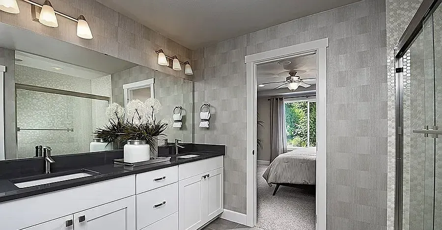 Bathroom with white cabinets, dark countertop, large mirror, and open doorway to bedroom.