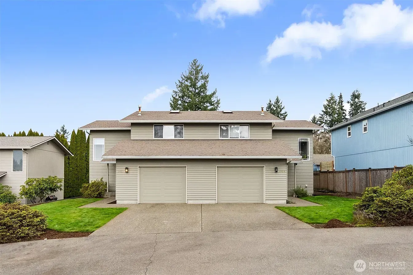 Suburban townhouse with beige siding, double garage, and a driveway under a blue sky