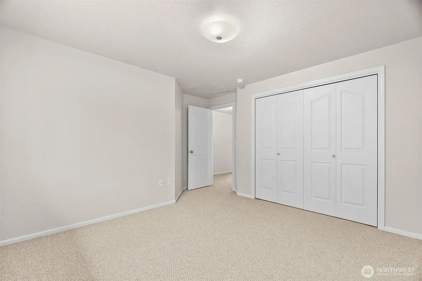 Empty beige bedroom with carpet, white walls, and closet doors on the right