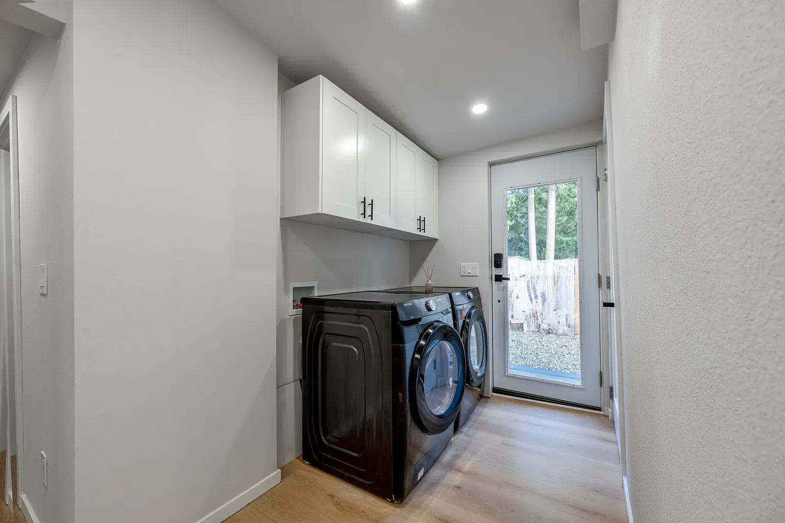 Narrow laundry room with white cabinets, washer and dryer, and a glass door to outside.