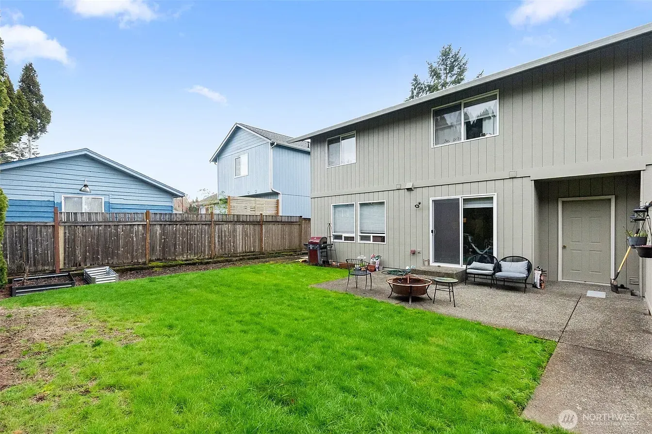 Backyard with green lawn, wooden fence, and two-story gray house with patio doors and gravel walkway