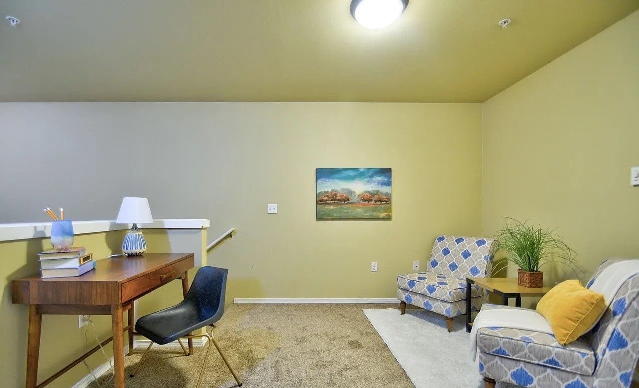 Loft with desk, chairs, rug, and artwork. Olive green walls, tan carpet.