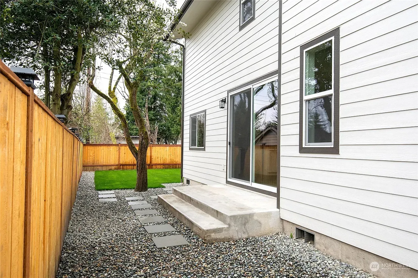 Backyard with white house, sliding glass door, stone path, wooden fence, tree, and steps.