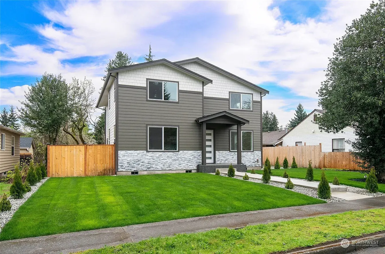 Two-story house with gray siding, light stone, and green lawn, under blue sky with a few clouds.