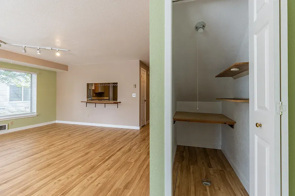 Empty living room with wood floors and a peek into a small closet with shelves and a hanging rope.