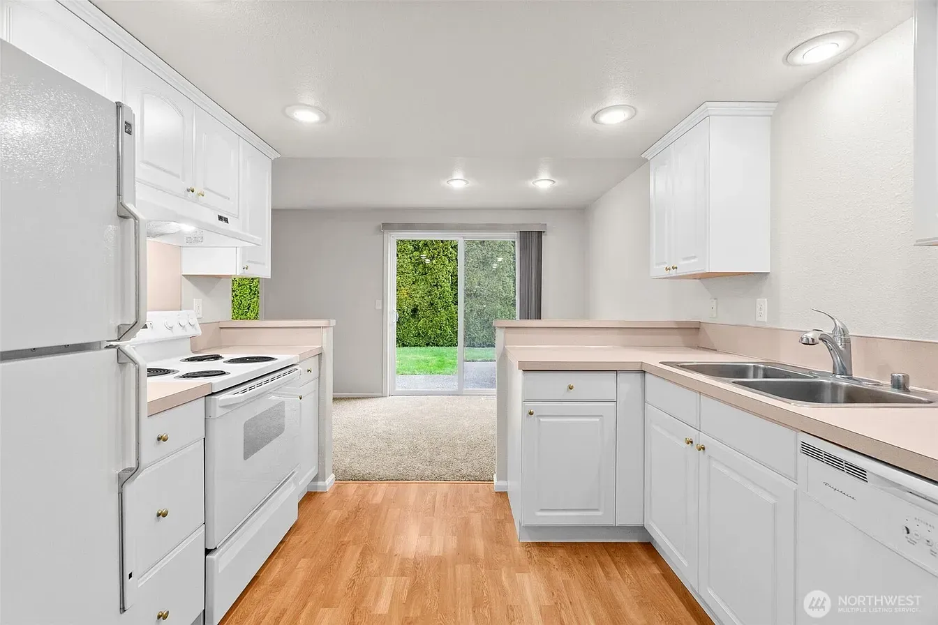Bright white galley kitchen with wood floors and sliding glass doors to a green backyard