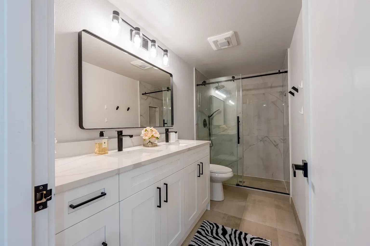 Bright modern bathroom with white vanity, large mirror, and glass-enclosed shower.