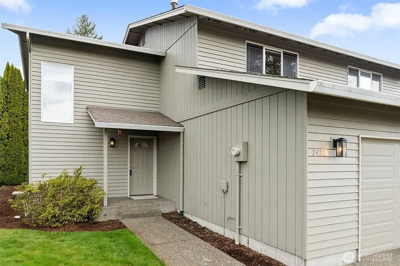 Exterior of a beige townhouse with a garage, front entry, and small gravel walkway