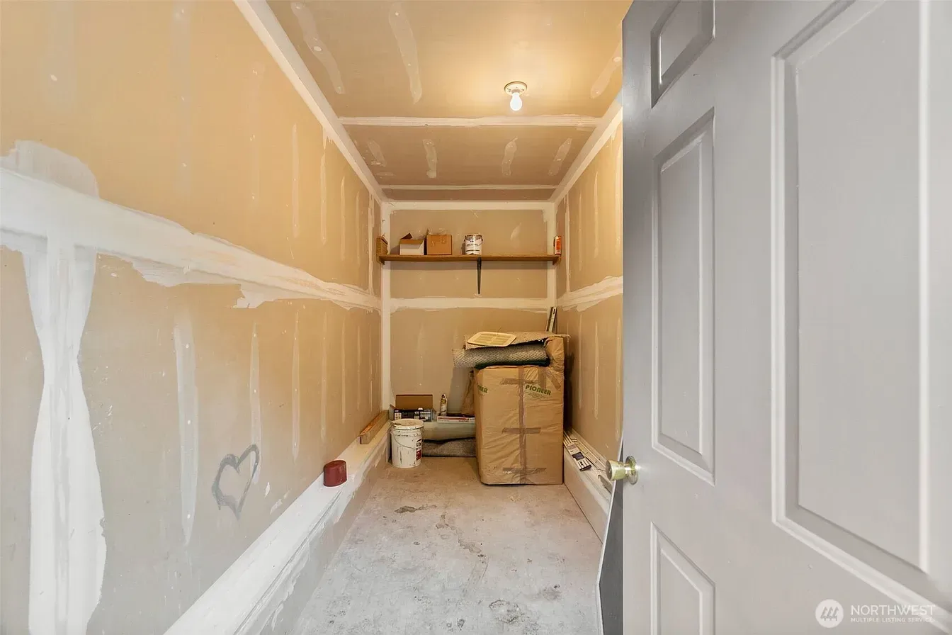 Narrow unfinished hallway with drywall patches, boxes, and a white door at the end of a construction site.