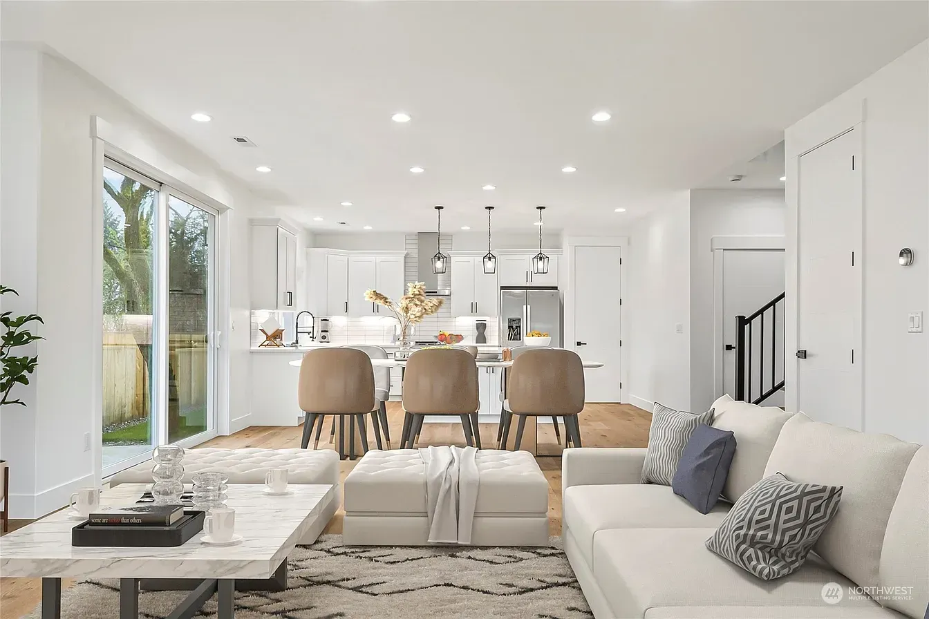 Bright open-concept living space with white walls, kitchen with island, seating, and a sliding glass door to a patio.