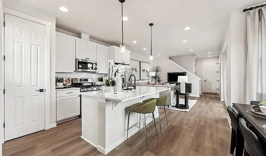 Modern white kitchen with island, seating, and stainless appliances; wood floors.