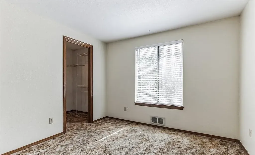 Empty room with floral carpet, a window with blinds, and a closet.