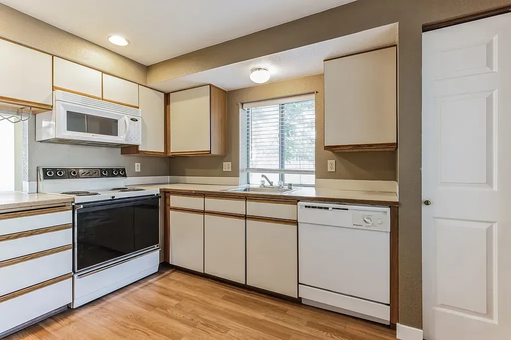 Kitchen with white cabinets, appliances, and light wood floors.