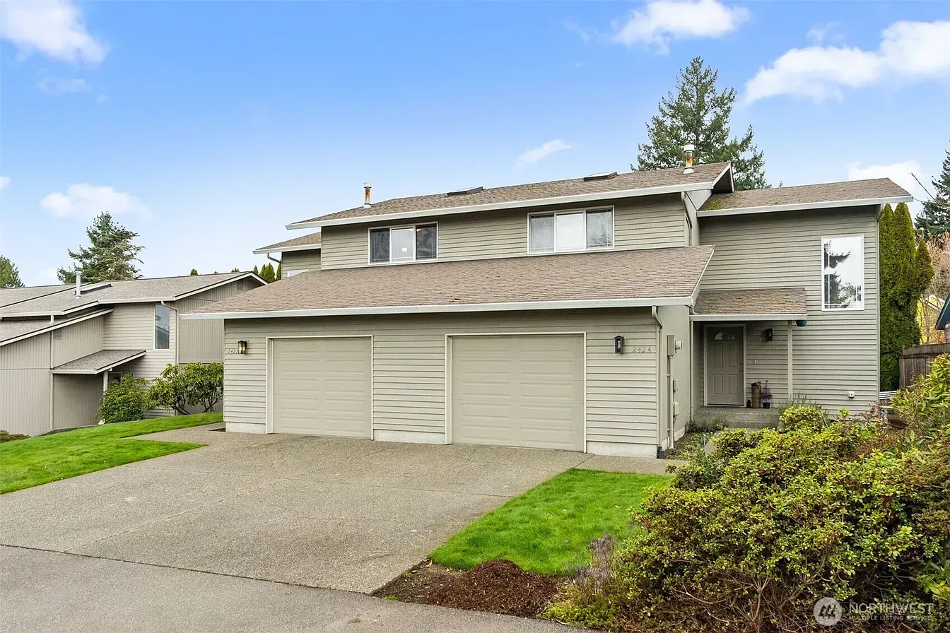 Suburban two-story beige house with garage, driveway, and front lawn under cloudy sky
