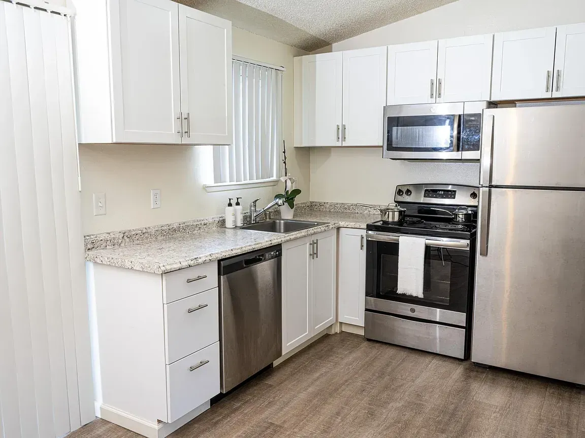 White kitchen with stainless steel appliances, cabinets, and a granite countertop.