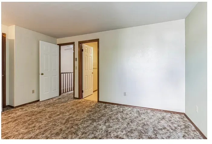 Empty room with brown carpet, white walls, and three doorways.