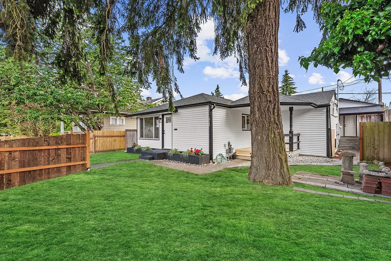 Backyard with green lawn, wooden fence, large tree, and a white shed under a cloudy sky