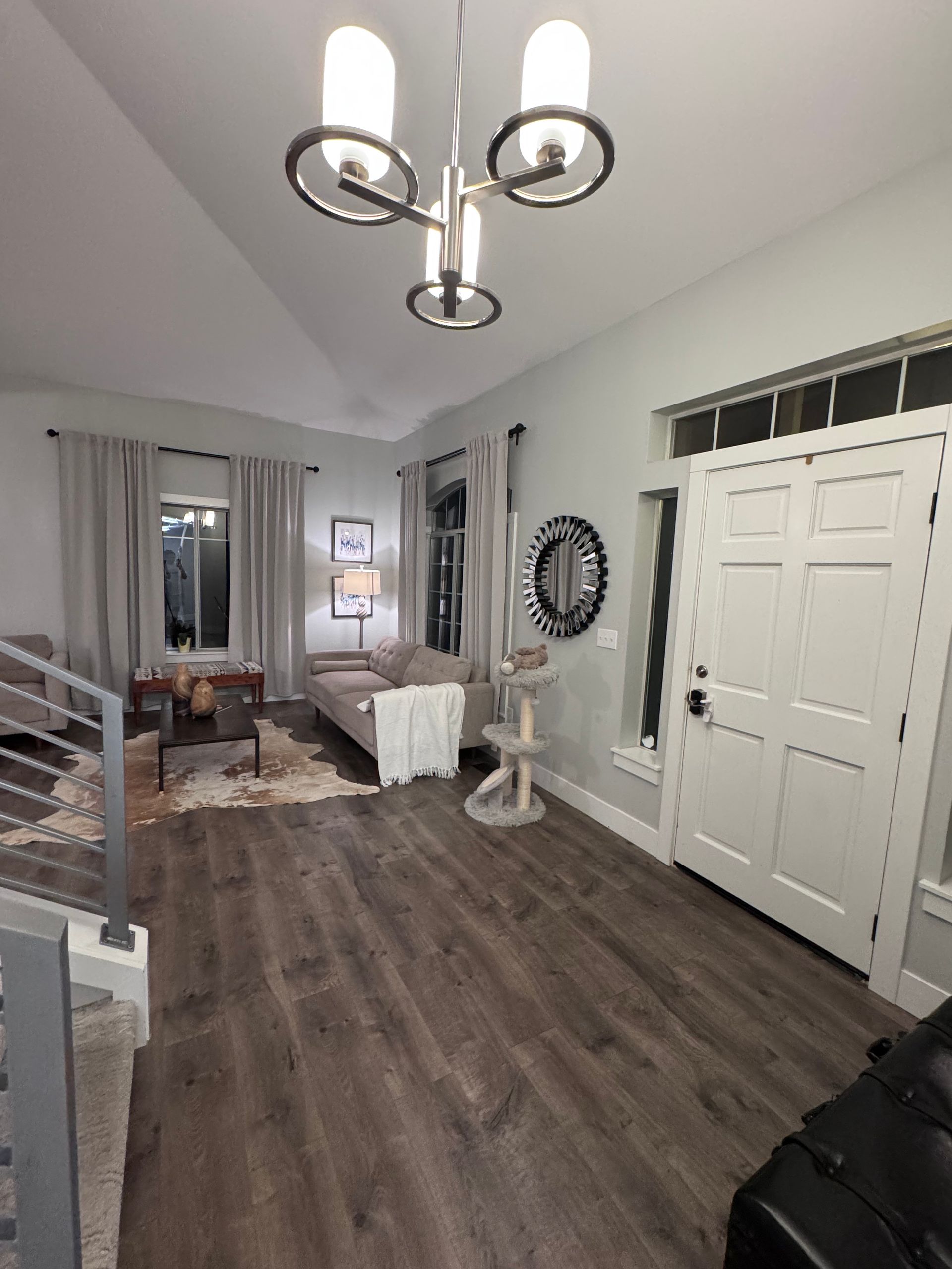 Living room with gray walls, wood floors, sofa, cat tree, chandelier, and a white front door.