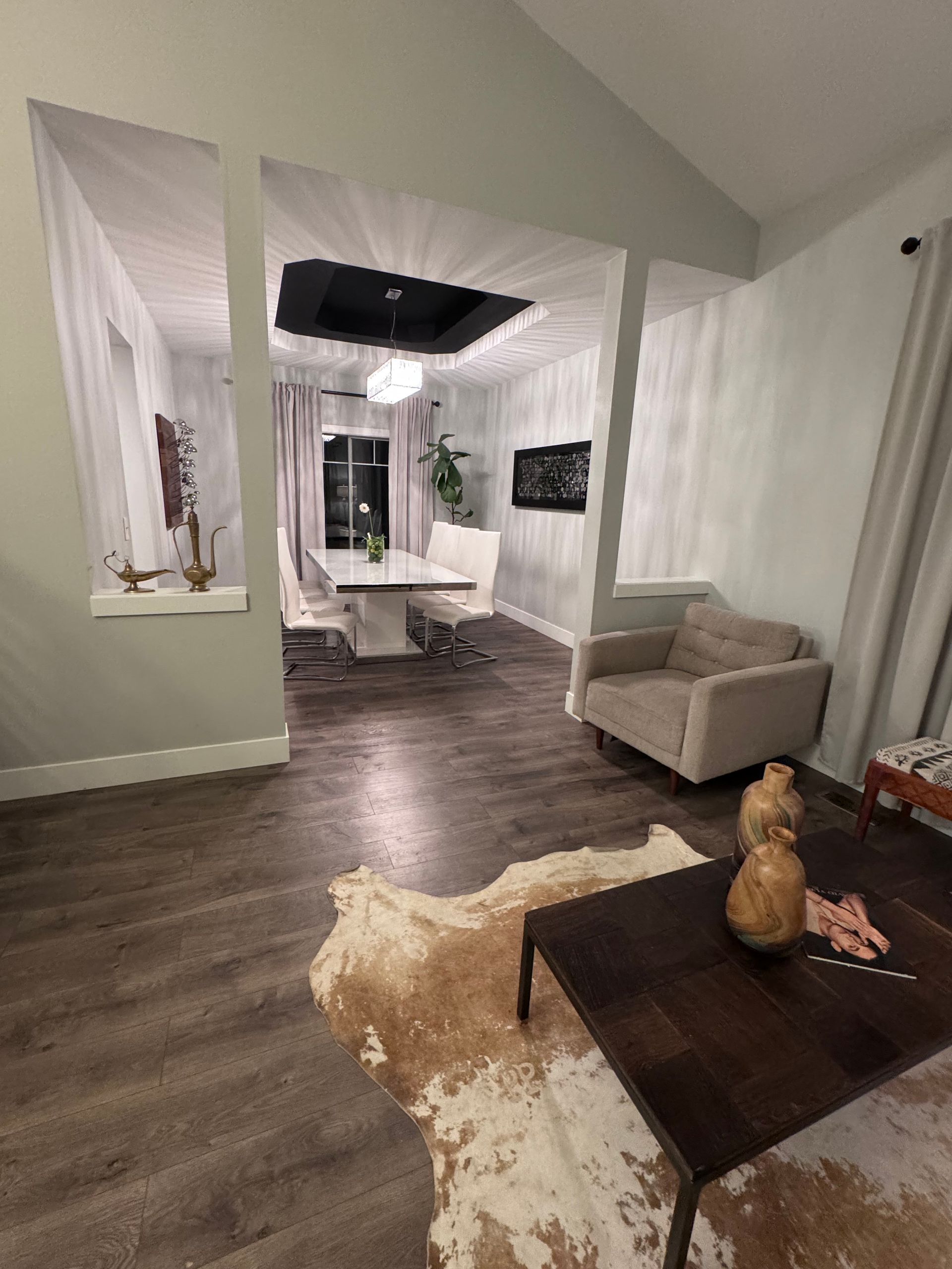 Living room with dining area visible, featuring wood floors, neutral walls, and a cowhide rug.