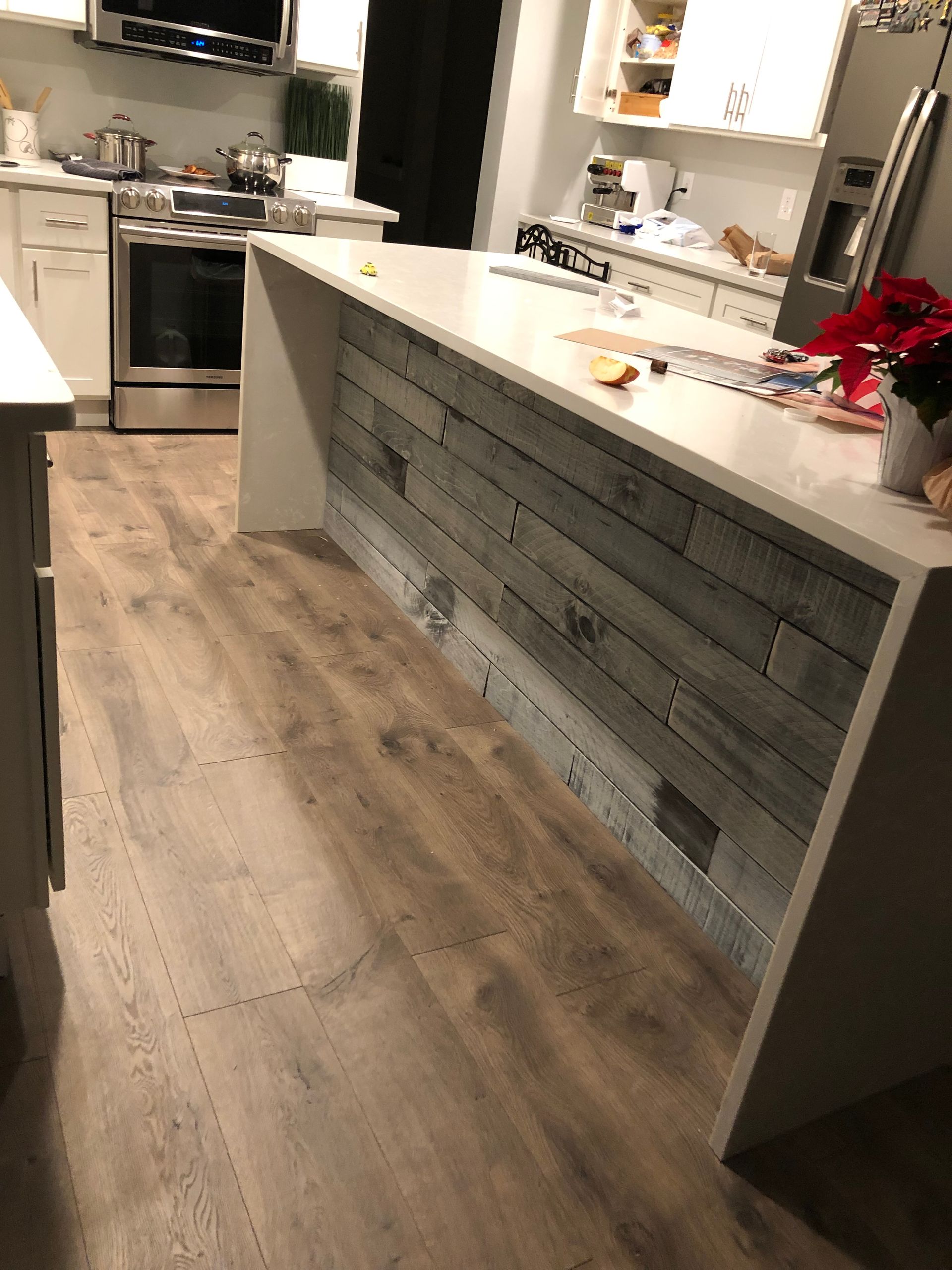 Kitchen with a white countertop island and wood-paneled siding; light wood flooring.