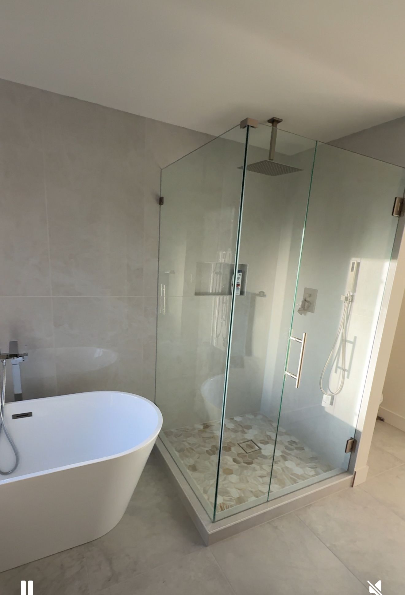 Modern bathroom with a glass shower and freestanding bathtub. Light grey tiles and neutral colors.