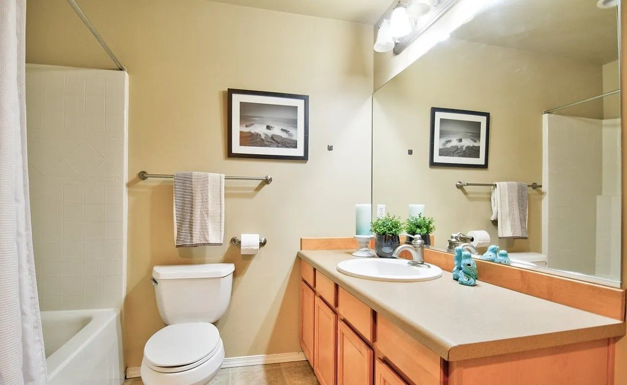 Bathroom with a toilet, vanity, bathtub, and mirror reflecting the room. Soft yellow walls, wooden cabinets, and towels.