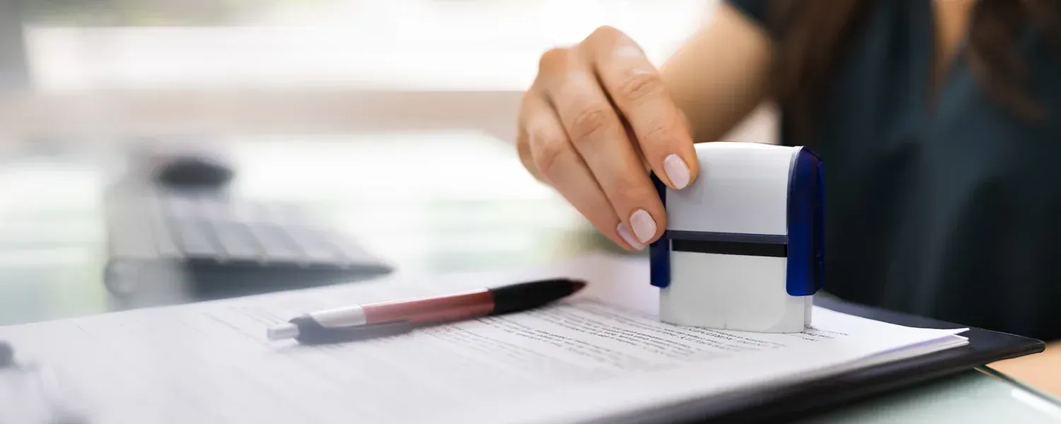 Person stamping a document with a rubber stamp on a desk with a pen and a keyboard.