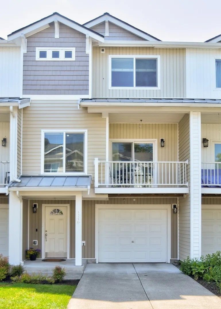 Townhouse with beige siding, white trim, and a garage door. Blue sky overhead.