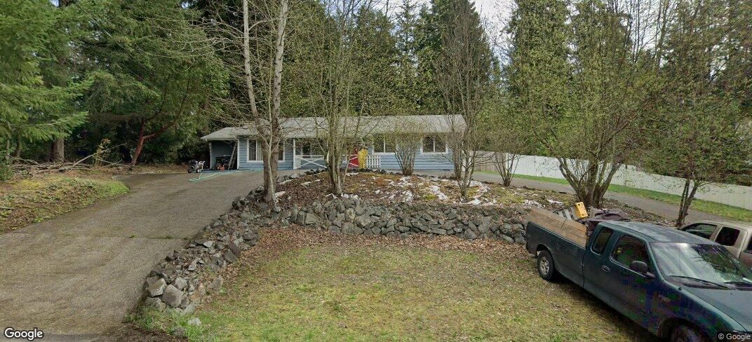 A light blue house sits amidst trees with a driveway leading to it, a truck parked nearby.