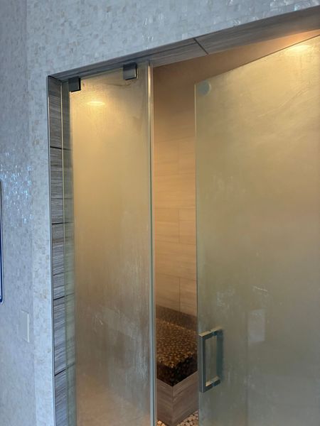 Shower with frosted glass door and a small bench inside. Gray and beige tones.