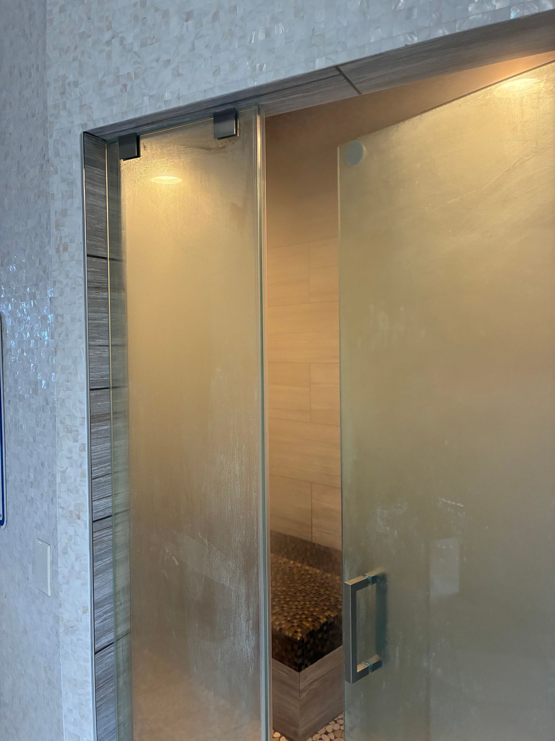 Glass shower door with textured glass. Stone tile walls and bench visible inside.