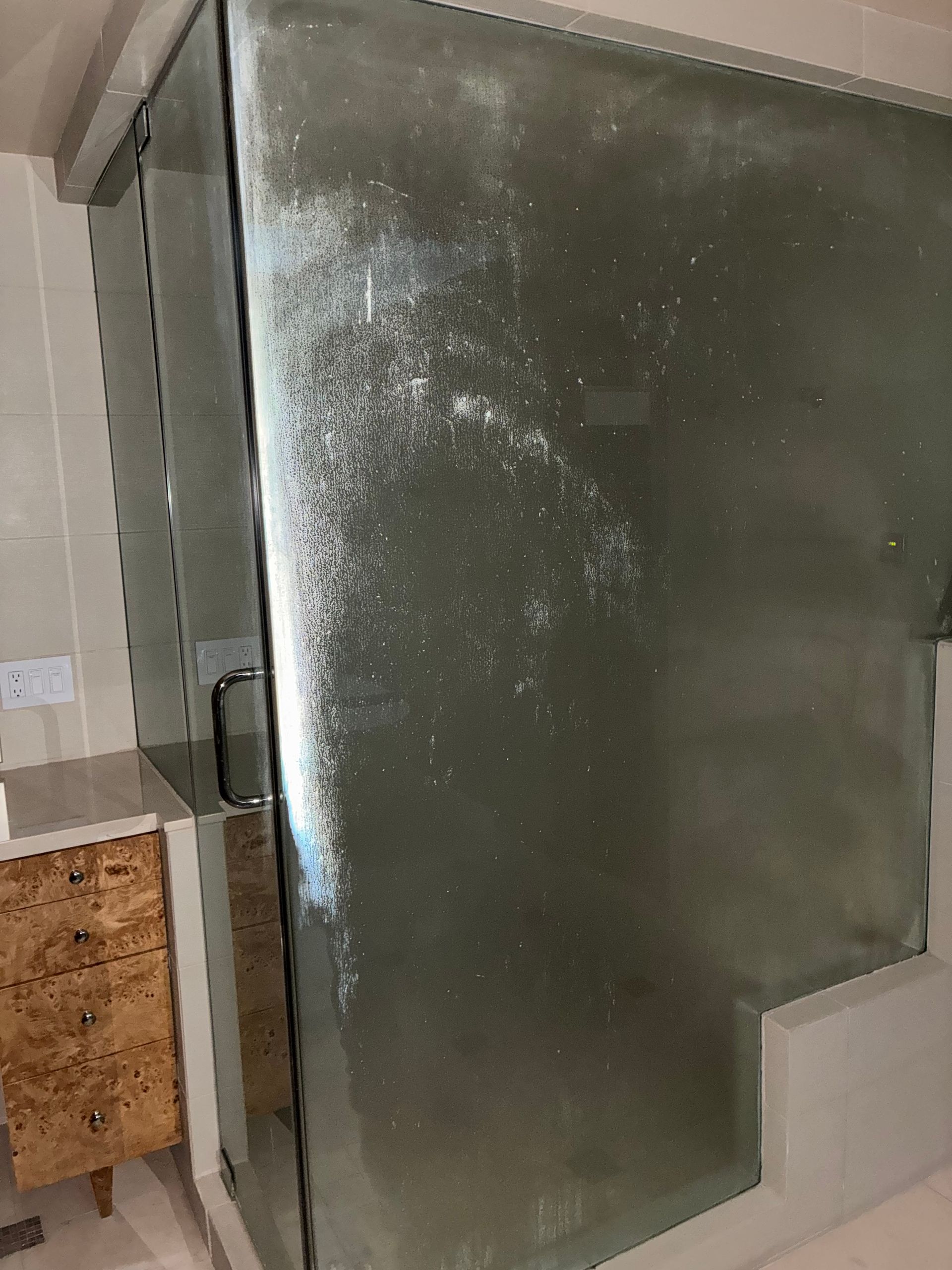Shower glass door with white mineral deposits.