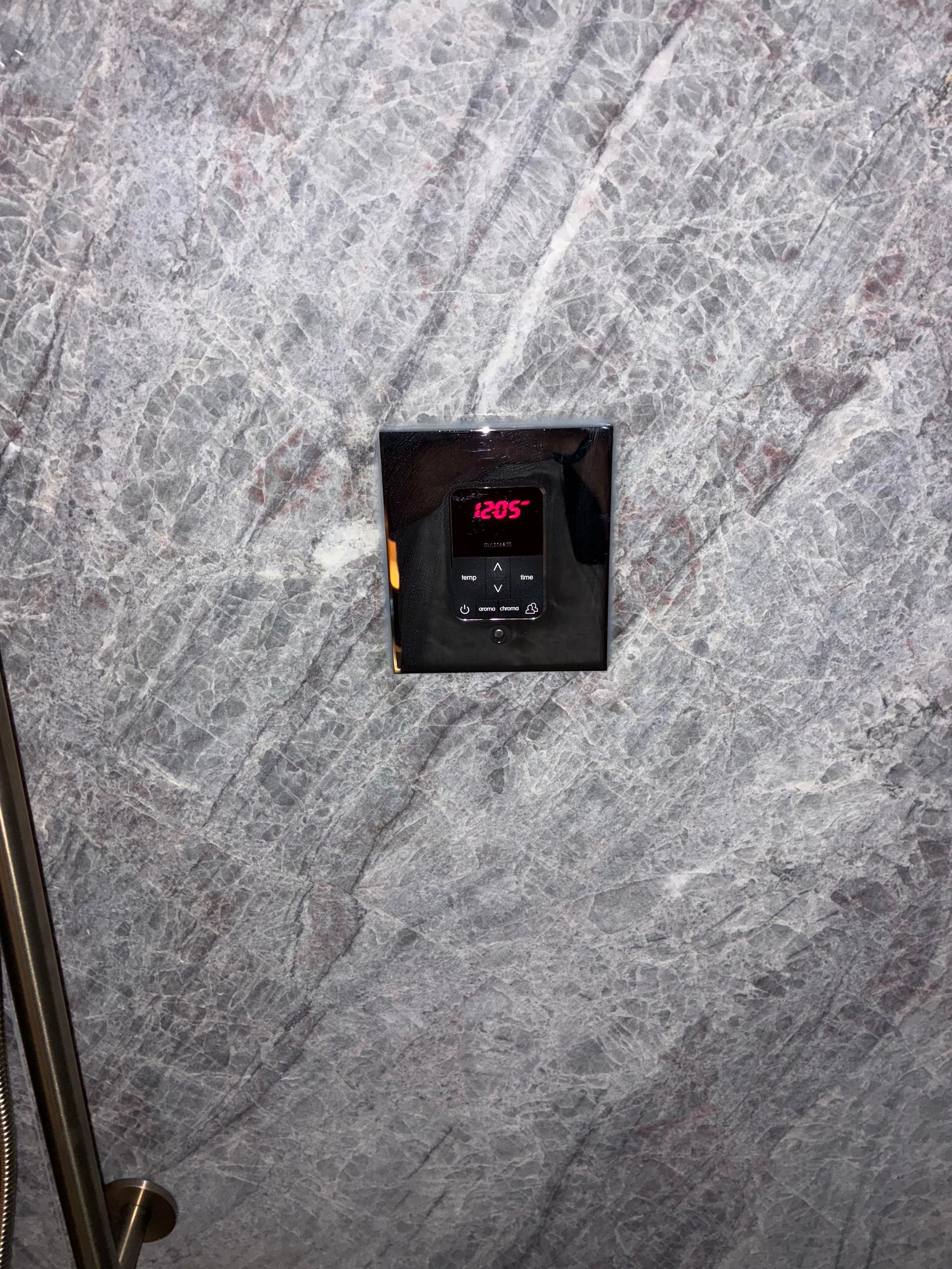 Black control panel with red display mounted on a gray marbled wall.