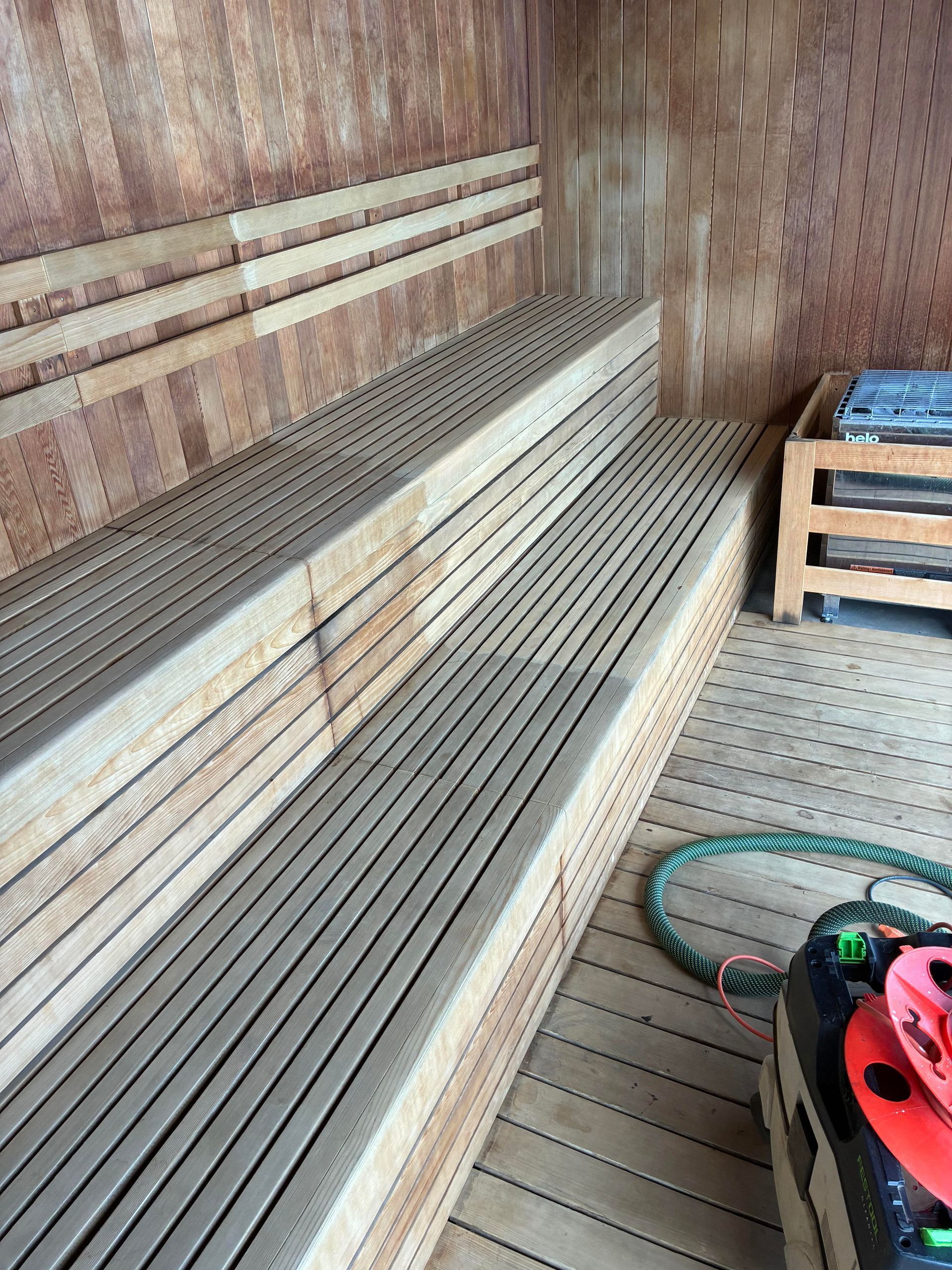 Wooden sauna interior with tiered benches, and a heater in the corner.