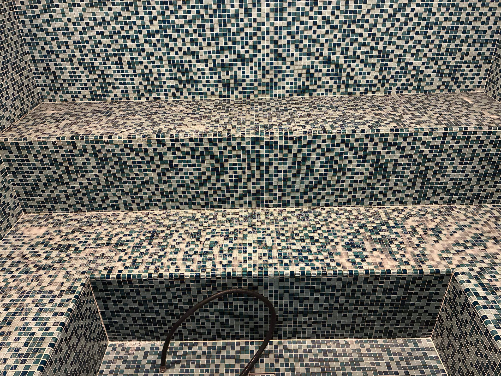 Mosaic-tiled steam room with three built-in benches, predominantly blue and white tiles.