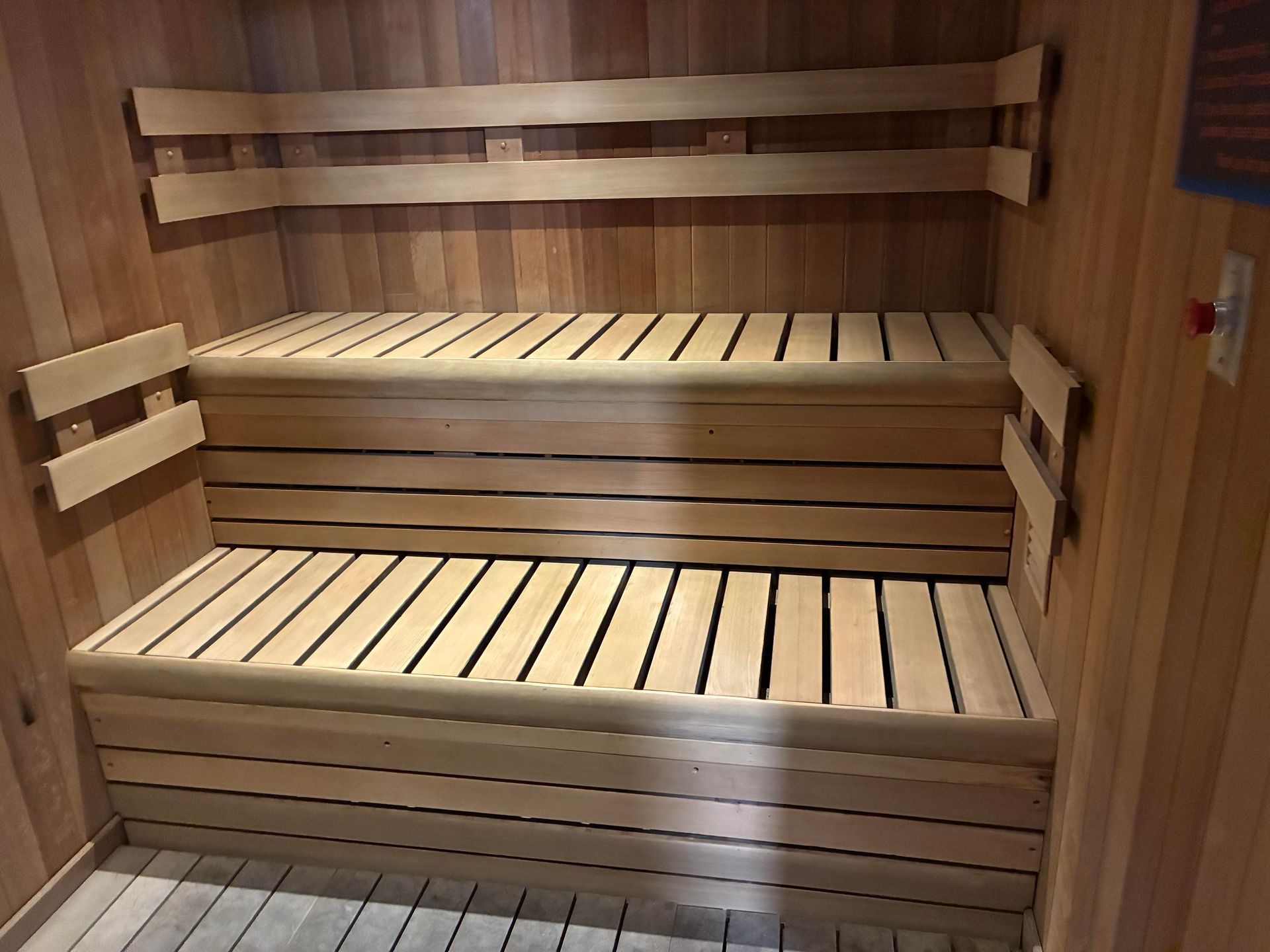 Wooden sauna interior with two-tiered benches. Light wood walls and seating.