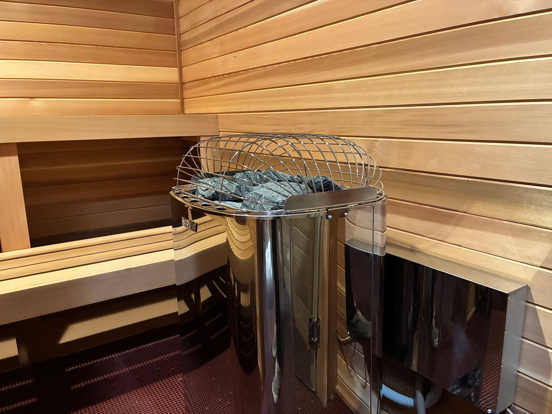 Interior of a wood-paneled sauna with a metal heater containing rocks, and bench seating.