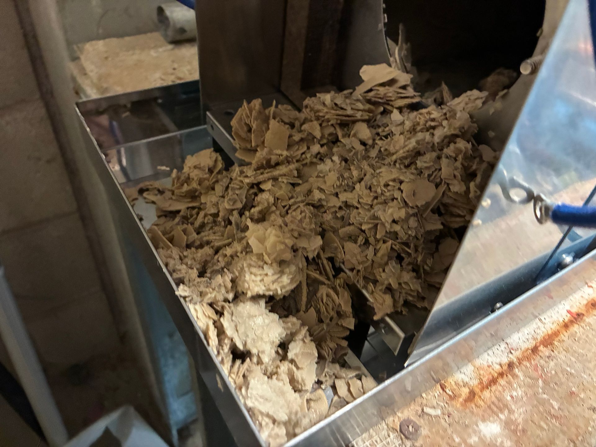 Shredded brown material in a metal trough, likely industrial processing.