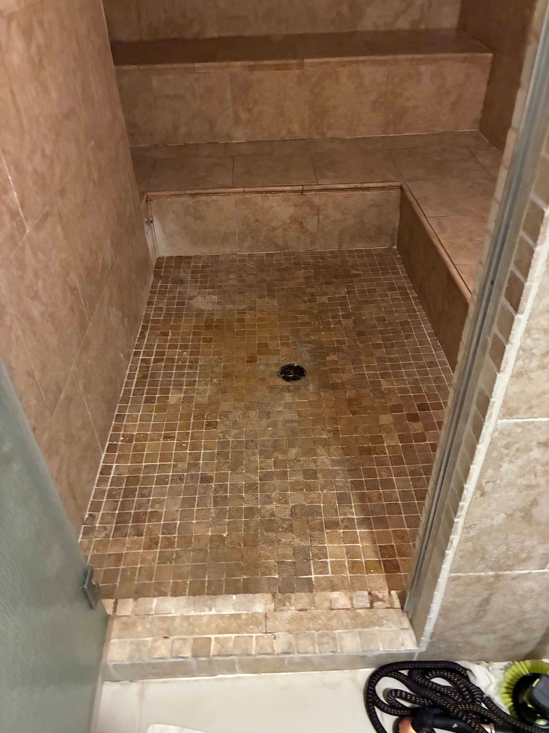 Tiled shower stall with a mosaic floor. A small step leads to a built-in bench. The drain is visible.