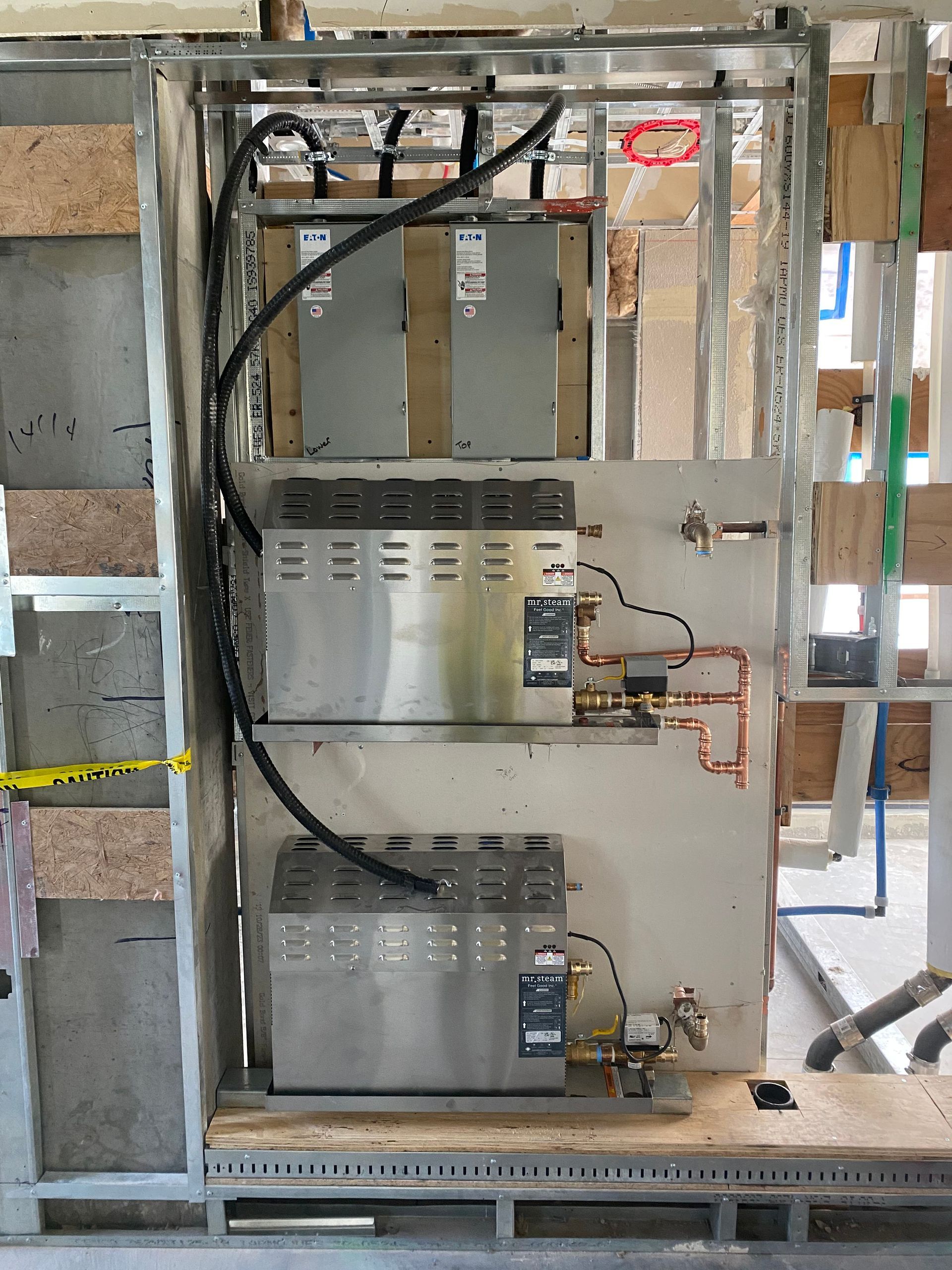 Electric water heaters and electrical components installed within a metal frame, mounted on a wall.