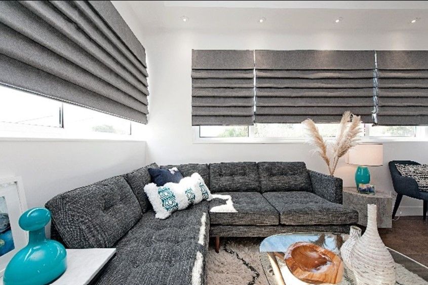 Grey fabric Roman shades installed on living room windows above a couch