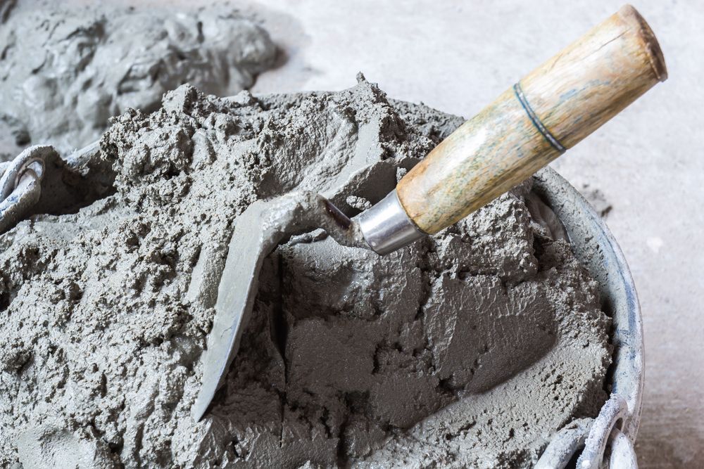 Trowel Resting in a Bucket of Wet Cement, Gray Color — Salisbury Concrete Contractors In Byron Bay, NSW