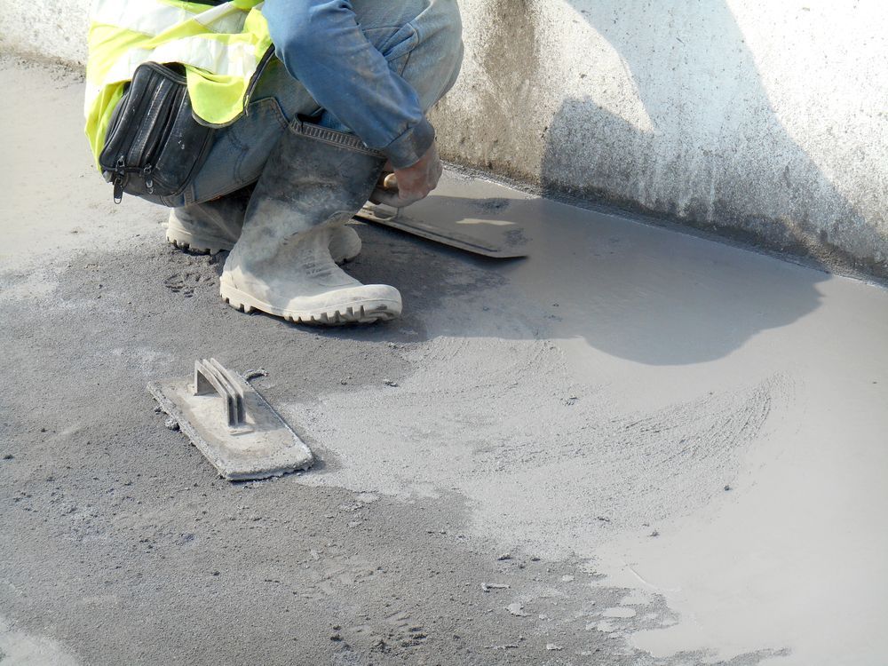 Construction Worker Smoothing Wet Concrete With a Trowel Near a Wall — Salisbury Concrete Contractors In Lennox Head, NSW