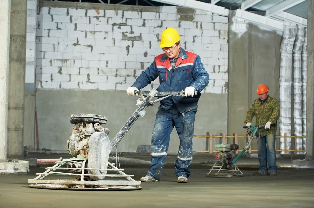 Two Construction Workers Smoothing Concrete With Power Trowels — Salisbury Concrete Contractors In Ocean Shores, NSW