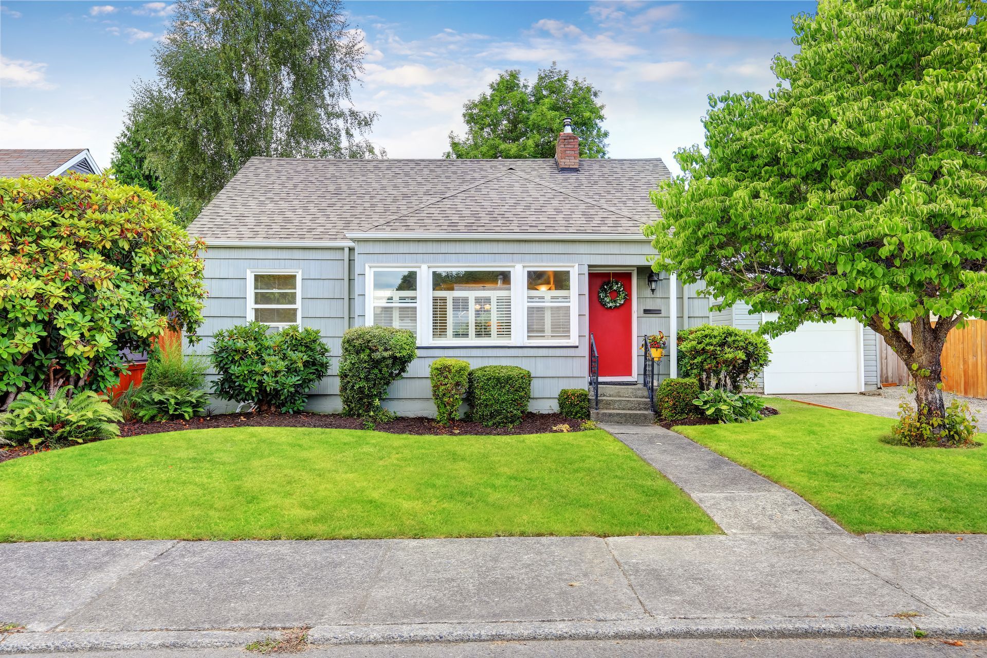 A small house with a red door and a lush green lawn.