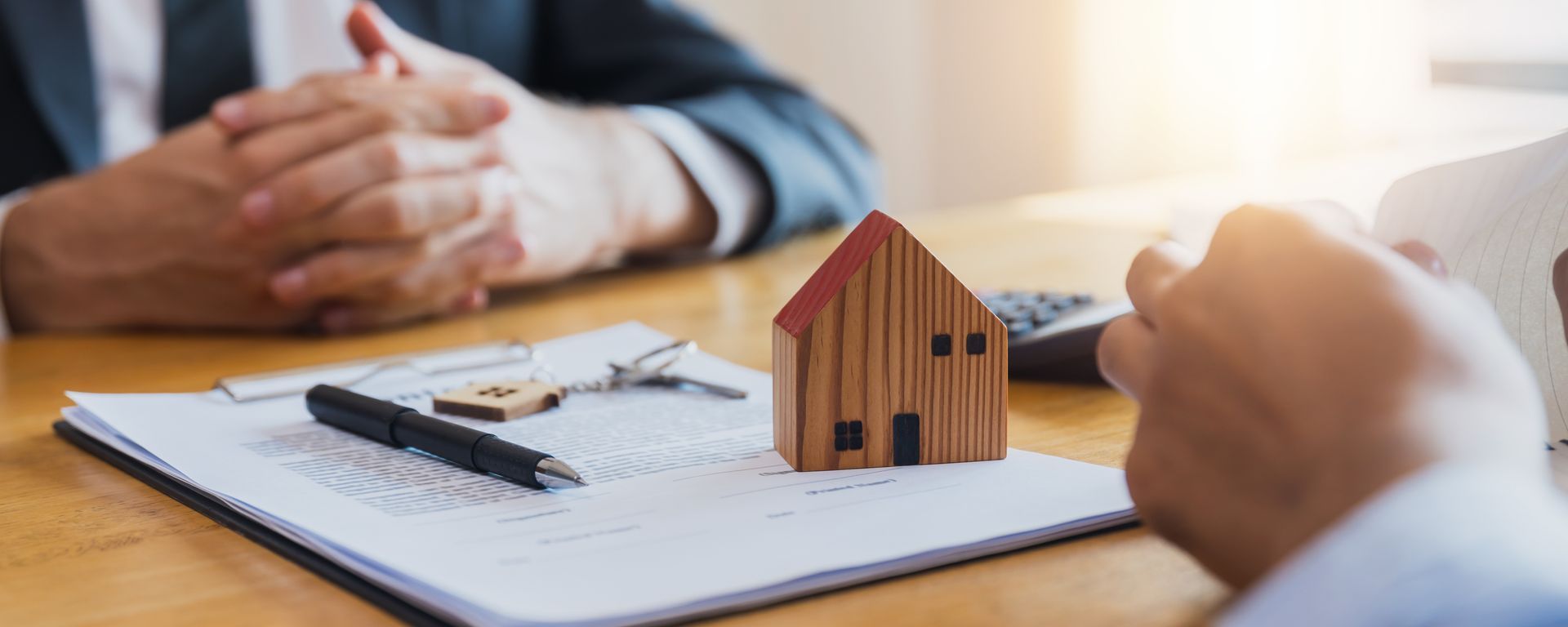 A man is sitting at a table with a model house and keys.
