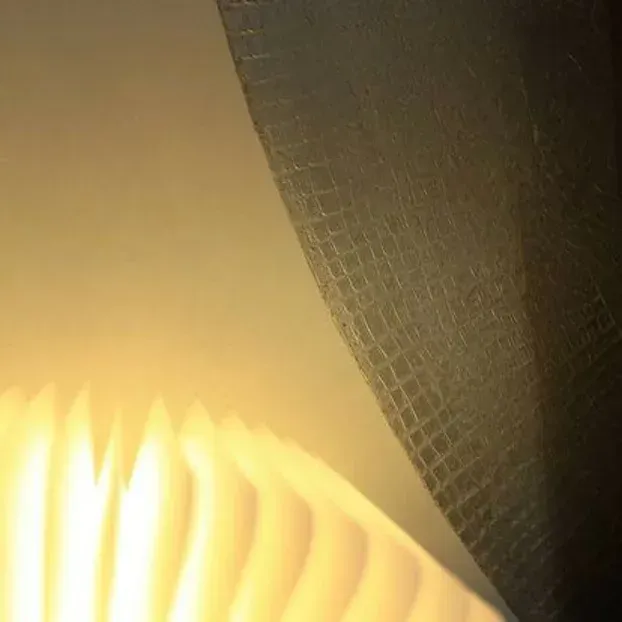 Una luce intensa, a fisarmonica, accanto a una tenda scura e strutturata, che illumina una parete chiara.