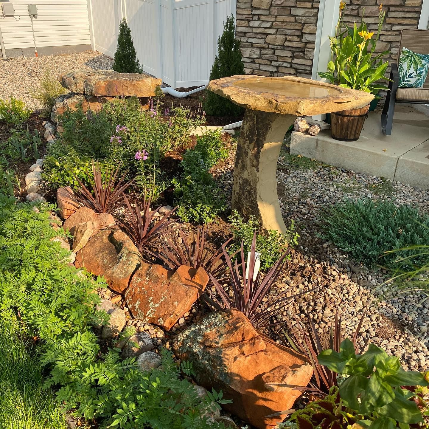 Landscaped garden with flowers, rocks, and a stone birdbath beside a patio