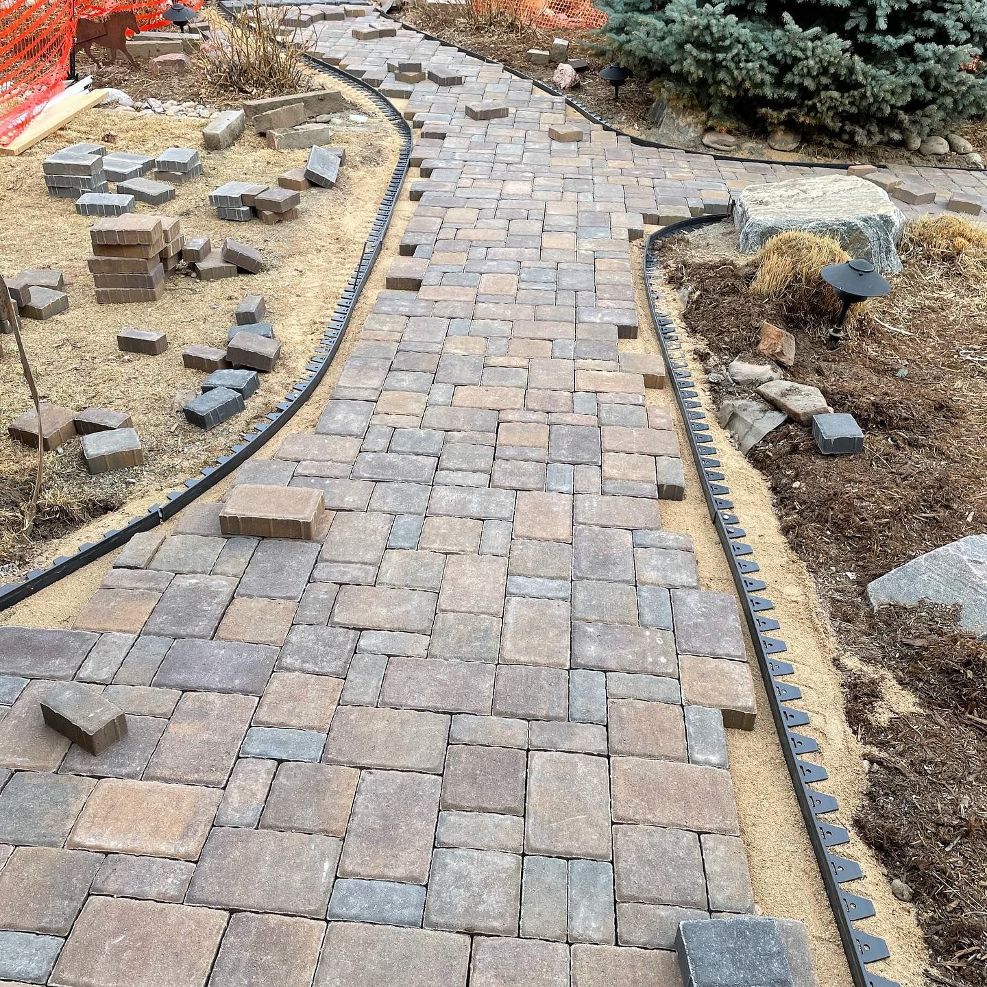 Curving brick paver walkway through a landscaped garden with stone edging and soil beds